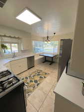 Kitchen with light tile patterned flooring, sink, a notable chandelier, white cabinetry, and appliances with stainless steel finishes