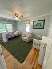 Bedroom featuring ceiling fan, ornamental molding, wood-type flooring, a textured ceiling, and a nursery area