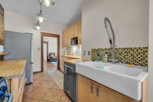 Kitchen featuring tasteful backsplash, light tile patterned floors, pendant lighting, stainless steel appliances, and sink