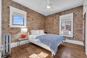 Bedroom featuring ceiling fan, radiator, cooling unit, brick wall, and dark wood-type flooring