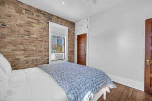 Bedroom with brick wall, cooling unit, hardwood / wood-style floors, and ceiling fan