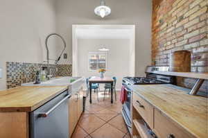 Kitchen featuring stainless steel appliances, butcher block counters, hanging light fixtures, and tasteful backsplash