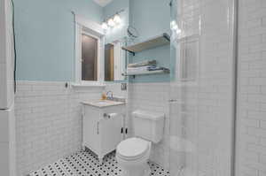 Bathroom featuring vanity, a shower with shower door, tile patterned floors, tile walls, and toilet