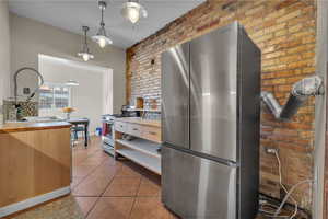 Kitchen featuring stainless steel appliances, brick wall, butcher block countertops, and decorative light fixtures