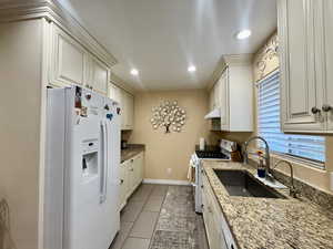 Kitchen featuring light stone countertops, white appliances, light tile patterned flooring, and single bowl sink and upgraded cabinets