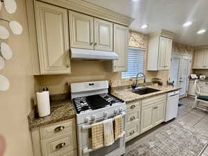 Kitchen featuring single bowl sink, upgraded cream cabinetry, white appliances, and granite countertops