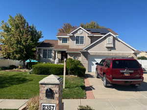 View of front facade featuring a garage, solar panels, and a front yard