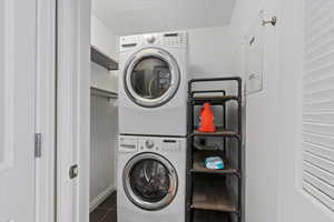 Washroom with dark tile patterned floors and stacked washer / drying machine