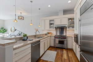 Kitchen featuring light stone counters, dark hardwood / wood-style floors, built in appliances, sink, and hanging light fixtures