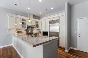 Kitchen featuring kitchen peninsula, built in appliances, dark wood-type flooring, and decorative light fixtures