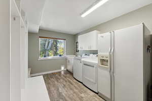 Washroom featuring light wood-type flooring, sink, washing machine and clothes dryer, and cabinets