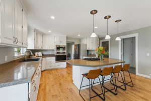 Kitchen featuring white cabinets, a kitchen island, stainless steel appliances, light wood-type flooring, and sink