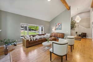 Living room with an inviting chandelier, light hardwood / wood-style flooring, beam ceiling, and high vaulted ceiling