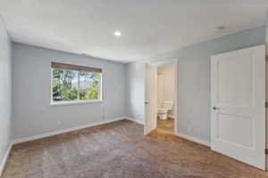 Unfurnished bedroom with light colored carpet and ensuite bathroom