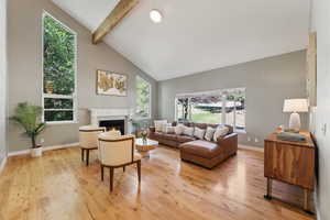 Living room with high vaulted ceiling, beam ceiling, light hardwood / wood-style floors, and a fireplace