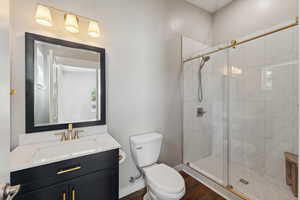 Bathroom with hardwood / wood-style floors, an enclosed shower, vanity, and toilet