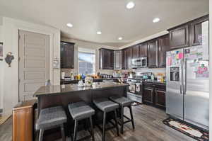 Kitchen with dark stone counters, a center island, a kitchen breakfast bar, stainless steel appliances, and dark hardwood / wood-style flooring