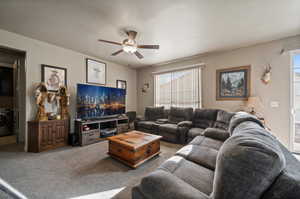 Carpeted living room with ceiling fan, a textured ceiling, and washer / dryer