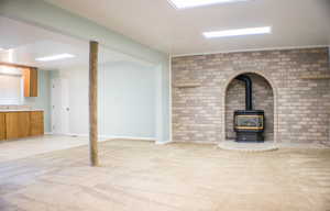 Unfurnished living room with brick wall, light colored carpet, sink, and a wood stove