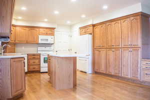 Kitchen with light wood-type flooring, sink, white appliances, and a center island