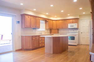 Kitchen featuring white appliances, light hardwood / wood-style floors, plenty of natural light, and a kitchen island