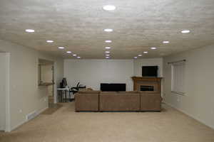 Living room featuring a tiled fireplace, a textured ceiling, and light colored carpet