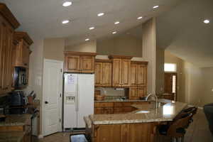 Kitchen featuring light tile patterned flooring, vaulted ceiling, black appliances, a center island with sink, and light stone countertops