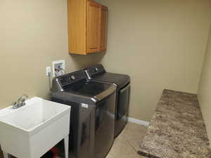 Laundry room with light tile patterned flooring, sink, washing machine and clothes dryer, and cabinets