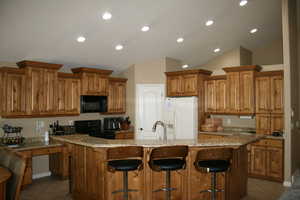 Kitchen featuring a kitchen island, lofted ceiling, tile patterned floors, and black appliances