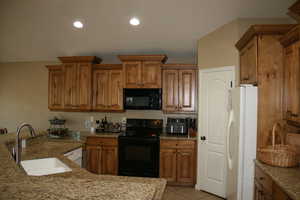 Kitchen with black appliances, light tile patterned flooring, sink, and light stone countertops