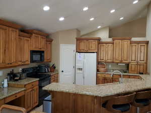 Kitchen with lofted ceiling, black appliances, a breakfast bar, and light stone countertops