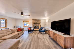 Living room featuring ceiling fan, a stone fireplace, light hardwood / wood-style flooring, and a wealth of natural light