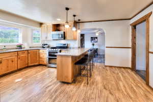 Kitchen with kitchen peninsula, a breakfast bar area, stainless steel appliances, light wood-type flooring, and decorative light fixtures