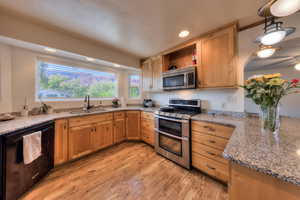 Kitchen with light wood-type flooring, sink, stainless steel appliances, and light stone counters