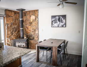 Dining area with ceiling fan, dark wood-type flooring, and a wood stove