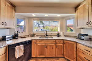 Kitchen featuring light stone counters, dishwasher, and sink