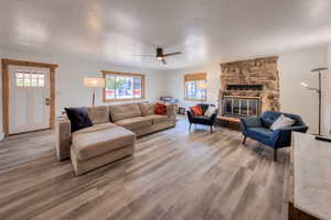 Living room featuring wood-type flooring, a stone fireplace, and ceiling fan