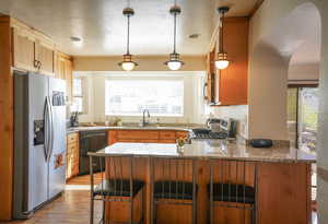 Kitchen with pendant lighting, kitchen peninsula, light hardwood / wood-style flooring, appliances with stainless steel finishes, and a breakfast bar area