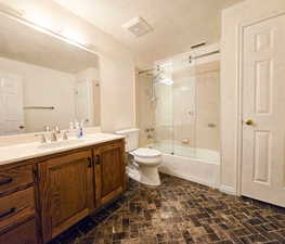 Full bathroom with combined bath / shower with glass door, vanity, and toilet