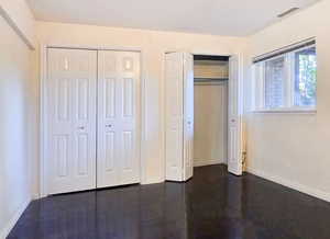 Unfurnished bedroom featuring double closet and dark hardwood flooring with a West window