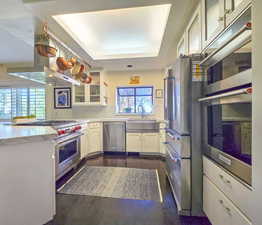 Kitchen with appliances with stainless steel finishes, white cabinetry, island range hood, kitchen peninsula, and sink