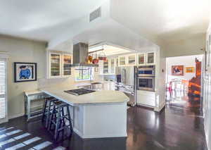 Kitchen featuring island range hood, white cabinets, stainless steel appliances, and kitchen peninsula