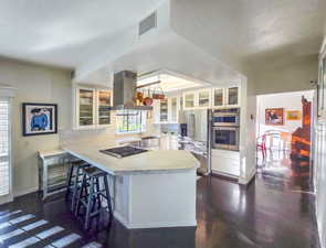 Kitchen featuring island range hood, white cabinets, stainless steel appliances, and kitchen peninsula