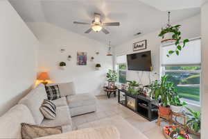 Living room with lofted ceiling, ceiling fan, and light tile patterned floors