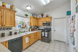 Kitchen with appliances with stainless steel finishes, vaulted ceiling, light tile patterned floors, a textured ceiling, and sink