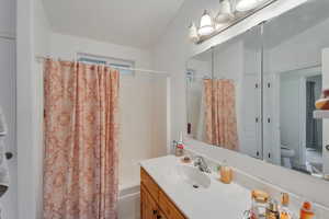 Full bathroom featuring shower / tub combo with curtain, vaulted ceiling, vanity, and toilet