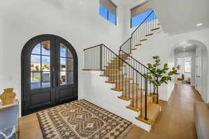 Foyer featuring a healthy amount of sunlight, a towering ceiling, light hardwood / wood-style floors, and french doors