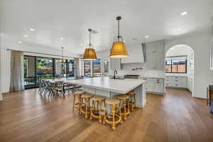 Kitchen with pendant lighting, light hardwood / wood-style floors, a large island with sink, and premium range hood