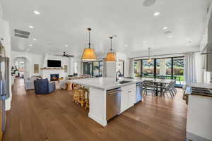 Kitchen featuring dark hardwood / wood-style floors, a kitchen island with sink, white cabinets, hanging light fixtures, and stainless steel dishwasher