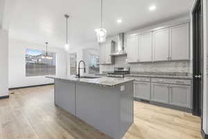 Kitchen featuring an island with sink, wall chimney exhaust hood, pendant lighting, gas range, and sink